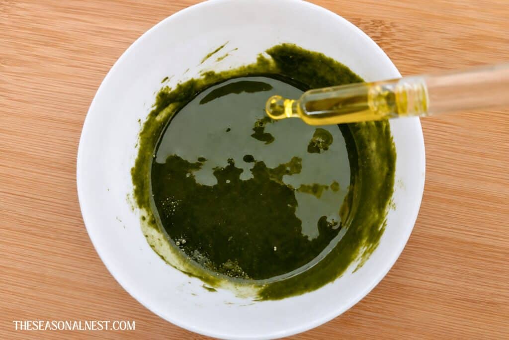 Adding oil with a dropper to green Matcha face mask in a bowl.
