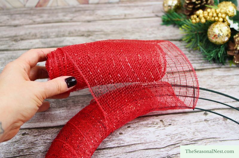 Close-up of a hand attaching red sparkly deco mesh to a metal wreath frame to start making a Christmas mesh wreath