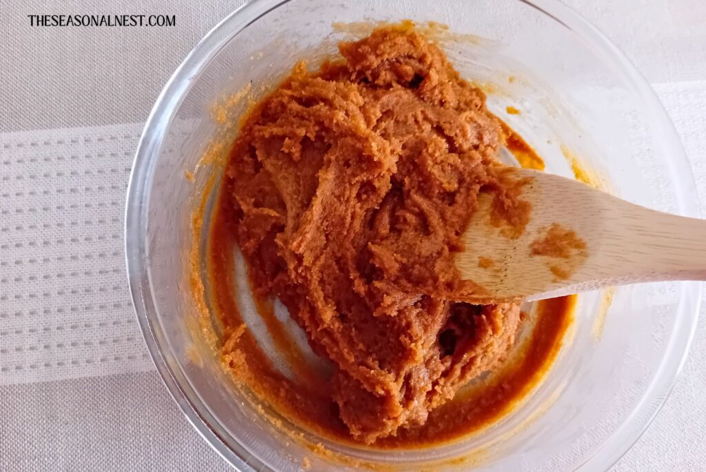 Thick peanut butter cookie dough being mixed in a glass bowl with a wooden spoon, showing a dense, slightly sticky texture.