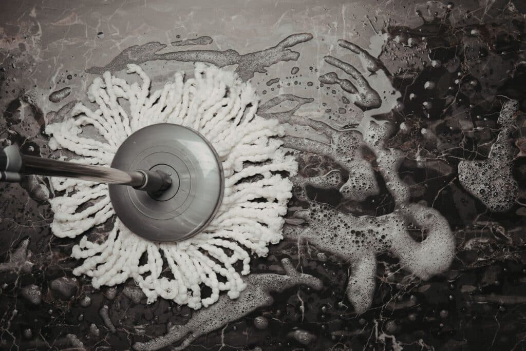 White mop head cleaning a dark floor surface with soap and water during deep house cleaning.