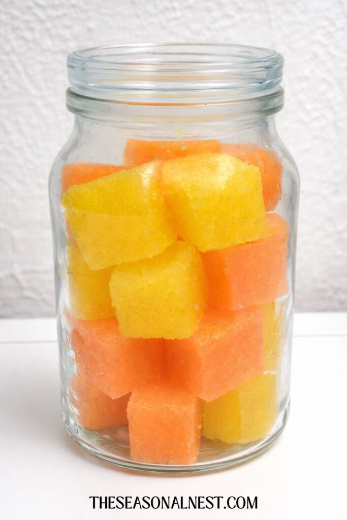 Lemon and orange sugar scrub cubes in a glass jar.