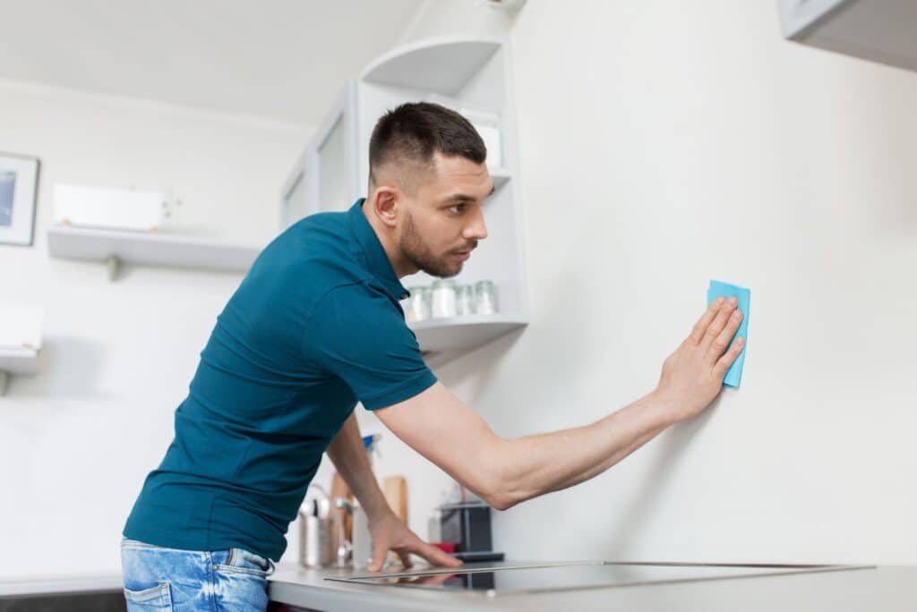 Man wiping scuff marks off a white wall with a cloth during spring cleaning.