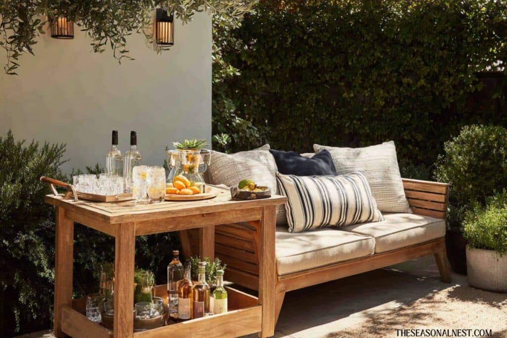 Wooden drinks cart with bottles and glasses next to outdoor bench seating in a backyard.