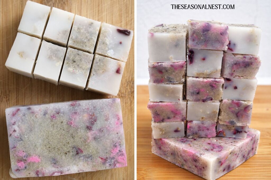 Stack of rose-sugar scrub cubes with pink petals and herbs on a wooden board, with additional cubes arranged beside them.